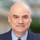 man wearing business suit and tie, standing outside. 