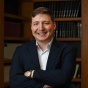 Man standing in front of sevearl bookshelves, smiling. 