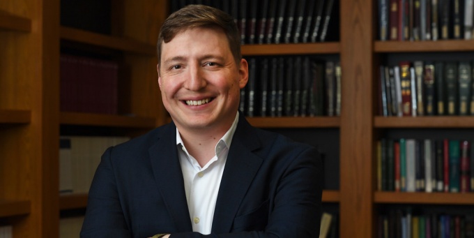 Man standing in front of sevearl bookshelves, smiling. 