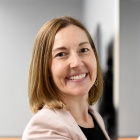 Woman smiling, standing and writing on a white board in a classroom.
