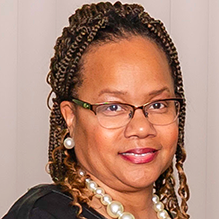 Woman with braided hair and glasses, smiling. 