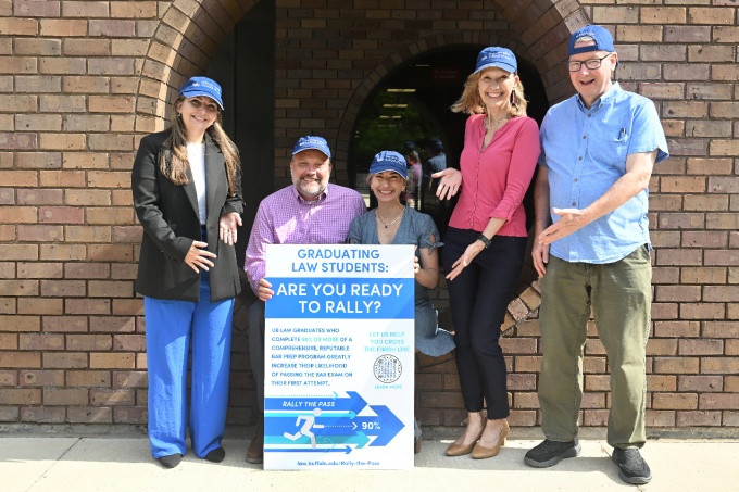 Group of people outside in front of a building, posing with a large poster.