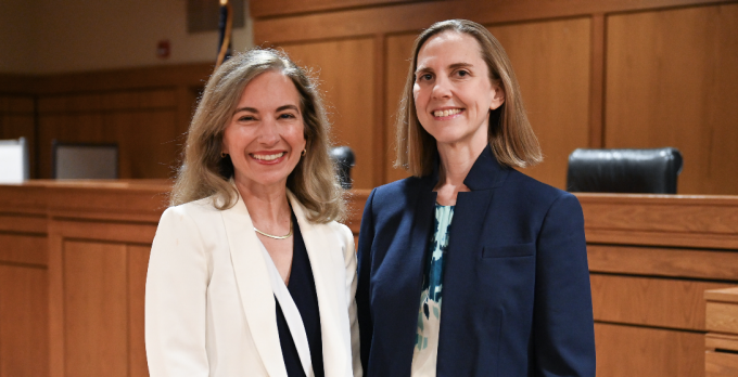 Two women, smiling, standing together in a courtroom.