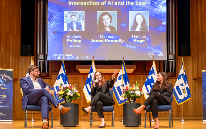 Three people sitting on a stage with large screen behind them that says Intersection of AI and the Law.