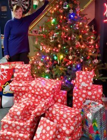 Decorated Christmas tree with colorful lights and ornaments, surrounded by a large stack of wrapped gifts in red and white snowflake paper, along with a few gift bags.