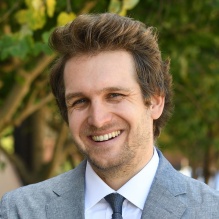 Linden-Retek wearing blue suit, standing outside next to O'Brian Hall, smiling.