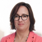 Allison Tam wearing peach colored jacket, beaded necklace, glasses, smiling.