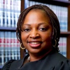 Justice King wearing a black judges robe, standing in front of bookshelves containing legal books.
