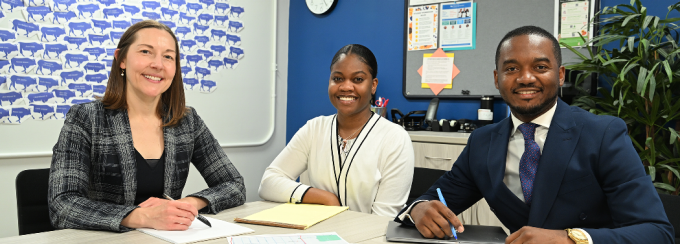 Three smiling people sitting at a table with papers on it. 