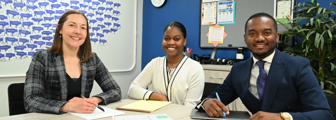 Three smiling people sitting at a table with papers on it.