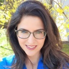 woman wearing glasses, standing outside, smiling. 