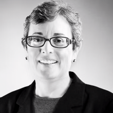 Black and white photo of woman wearing glasses, smiling. 