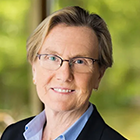 Woman wearing glasses, sitting in front of a window, smiling. 