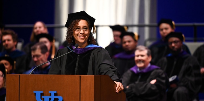 Woman on a stage, smiling, standing at a podium during UB School of Law Commencement. 