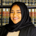 Naomi Goni standing in front of a bookcase with legal books, smiling,.
