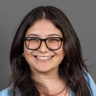 Elnara Karadzhayeva wearing blue top, glasses, smiling.