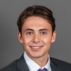 Aidan Comerford wearing grey jacket, purple tie, smiling.